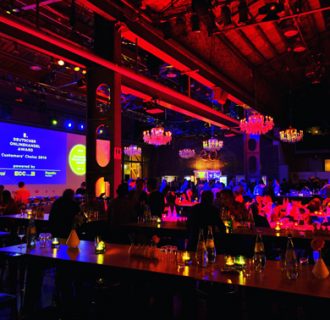 Professioneller Event DJ René Pera in den BALLONI Hallen/Köln beim Deutschen Online-Award. Die Gäste sitzen an blau/rot angestrahlten Tischen beim Networking.