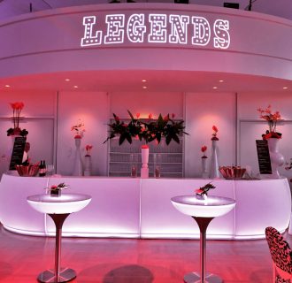 Professioneller Event-DJ René Pera bei einer Lounge-Veranstaltung im Festsaal/Flora/Köln. Man blickt auf eine stylisch inszenierte Bar mit dem Schriftzug "Legends" darüber.