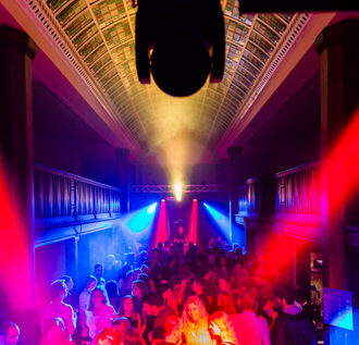 Professioneller Event DJ René Pera bei einer Party im Neptunbad/Köln. Man blickt von oben auf die volle Tanzfläche und sieht ihn am Ende des Raumes am Mischpult stehen.