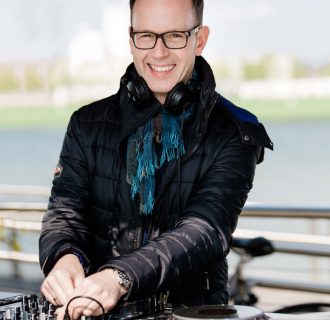 Professioneller Event DJ René Pera bei einer Open Air Lounge-Veranstaltung im Rheinauhafen/Köln. Er schaut direkt in die Kamera. Im Hintergrund sieht man den Rhein.